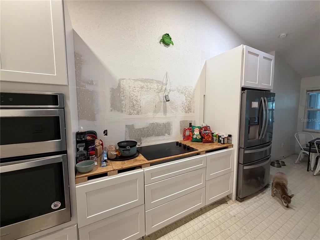A kitchen features white cabinets, a stainless steel oven, a refrigerator, and an unfinished backsplash — 5264 BRICKELL DRIVE, NORTH PORT, FL