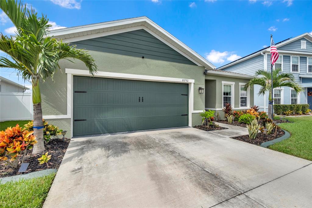 A green house with a two-car garage, a concrete driveway, and a palm tree — 8792 PRAIRIE CREEK DRIVE, NEW PORT RICHEY, FL