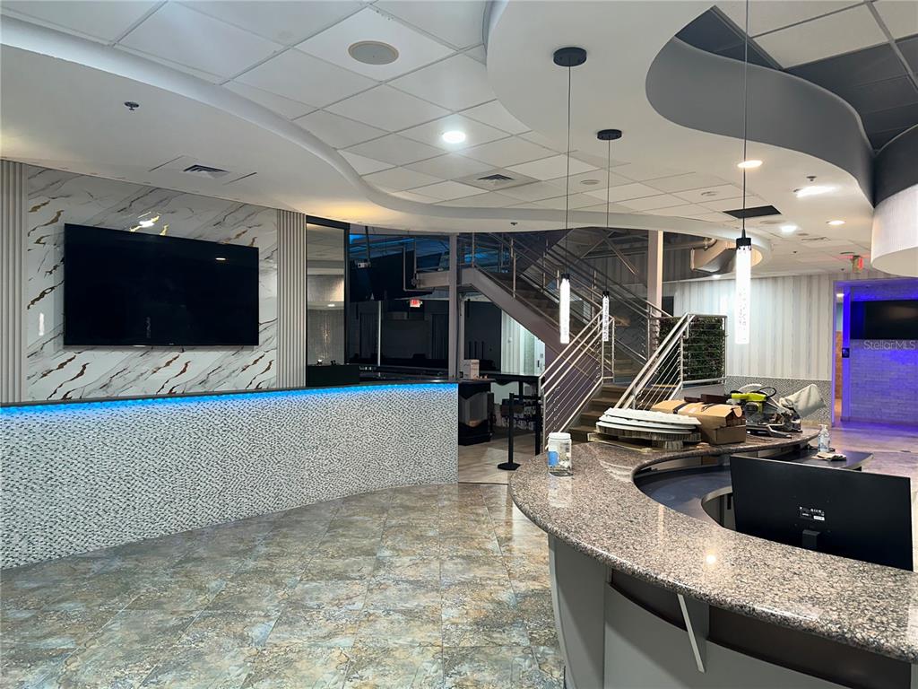 A modern reception area features a curved granite desk, marble wall accents, and a staircase — 6405 RALEIGH STREET, ORLANDO, FL