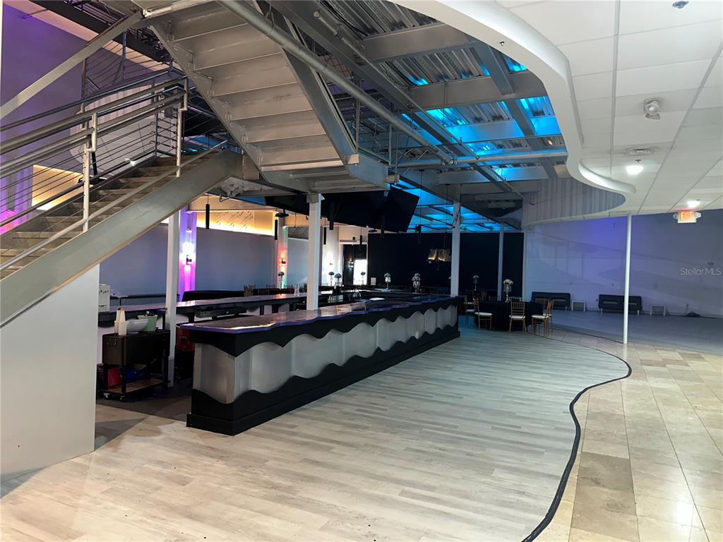 A modern event space features a large curved bar, metal staircase, and blue ceiling lighting — 6405 RALEIGH STREET, ORLANDO, FL