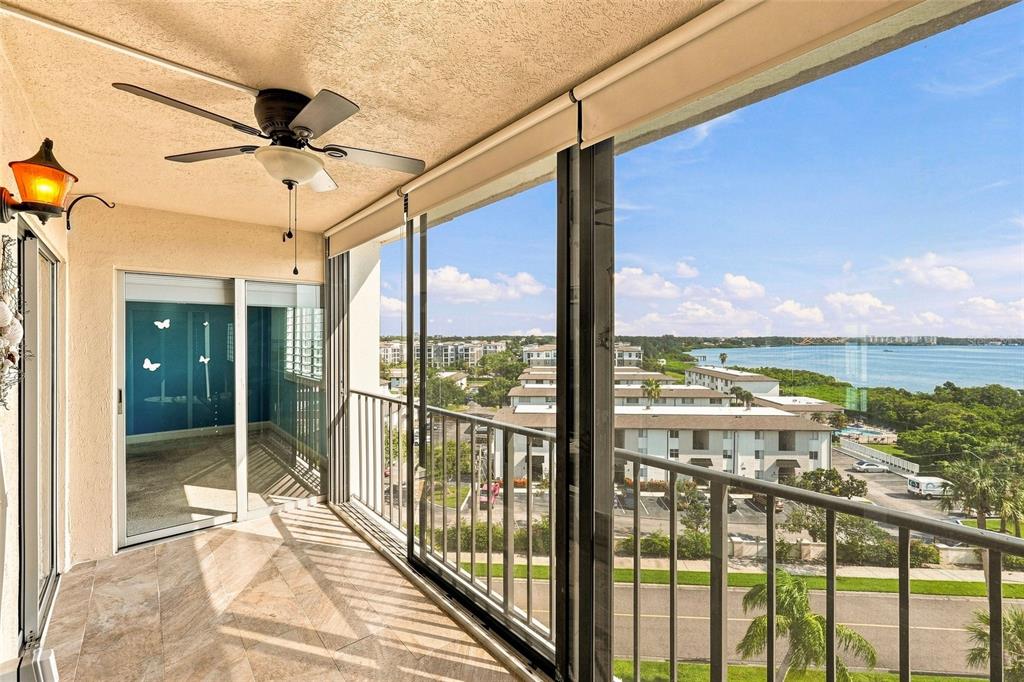 A tiled balcony with a ceiling fan overlooks a parking lot and a body of water — 19029 N US HIGHWAY 19 UNIT 9-704, CLEARWATER, FL