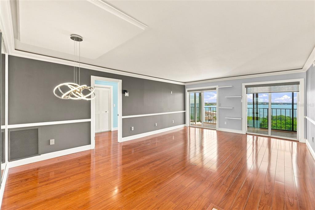 A living room with hardwood floors, gray walls, a modern chandelier, and sliding glass balcony doors — 19029 N US HIGHWAY 19 UNIT 9-704, CLEARWATER, FL