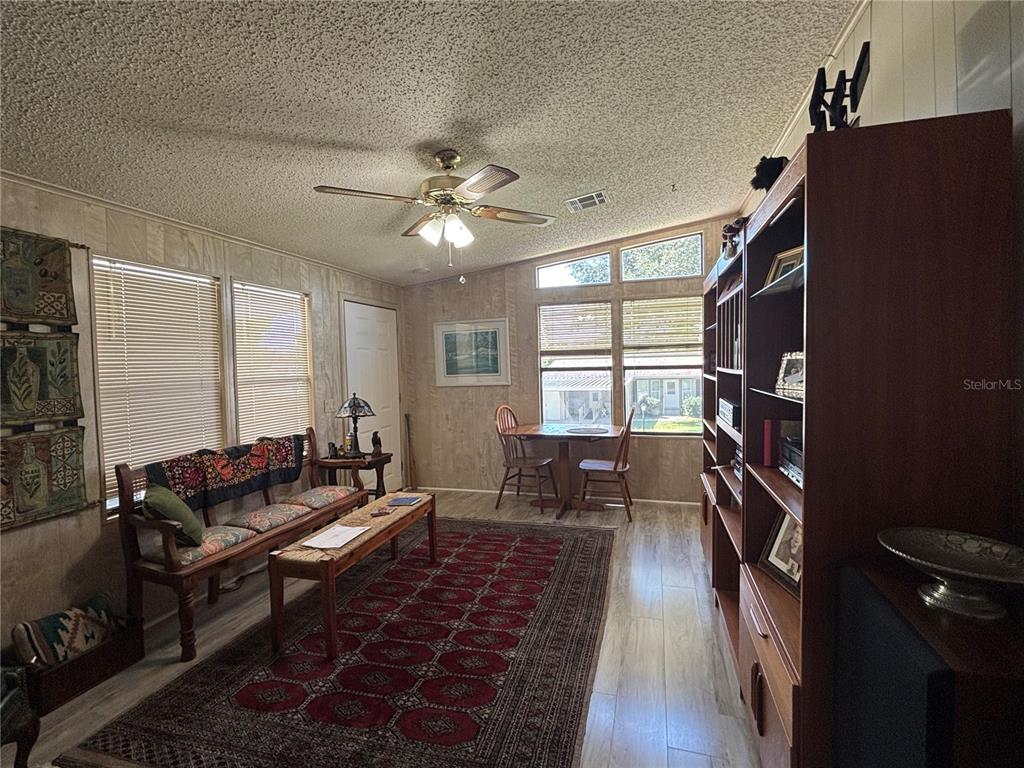 A living room features wood-paneled walls, a popcorn ceiling, a ceiling fan, and a red rug — 3725 COHEN DRIVE UNIT 717, ZELLWOOD, FL