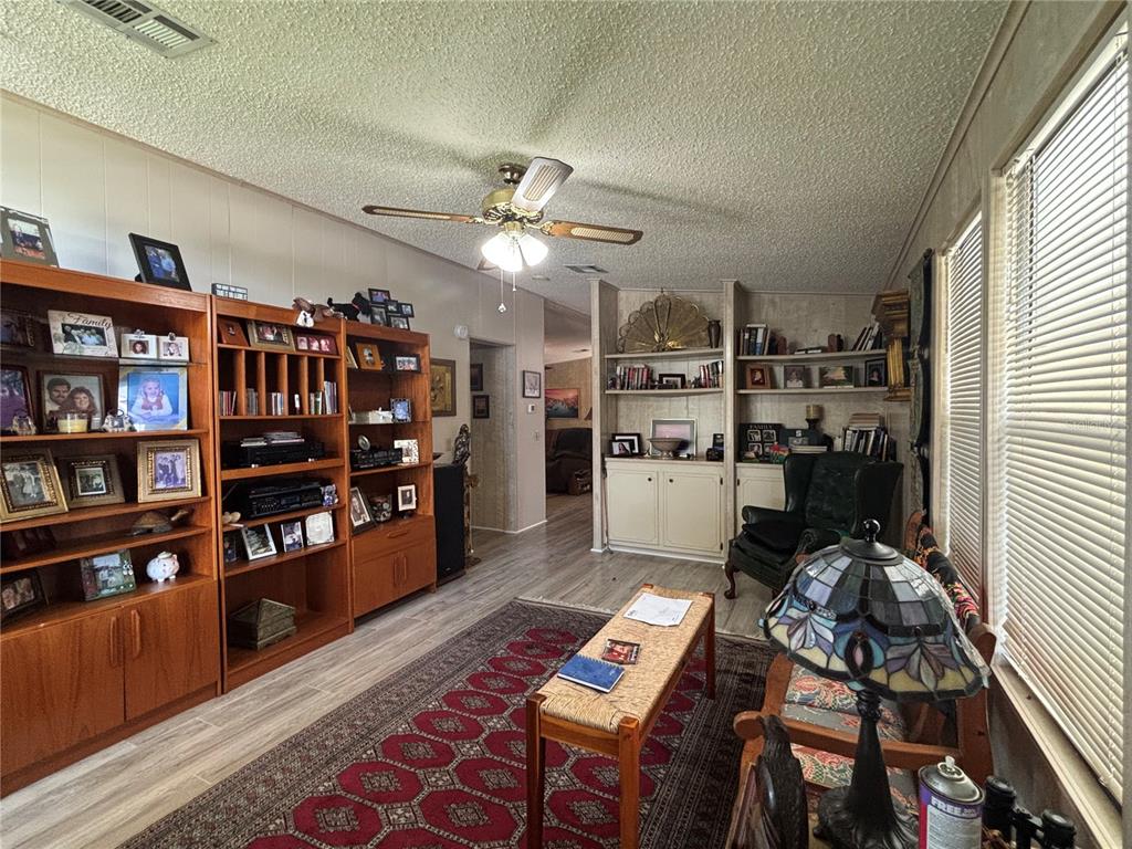 A living room features wood-look flooring, built-in shelving, a ceiling fan, and a patterned rug — 3725 COHEN DRIVE UNIT 717, ZELLWOOD, FL