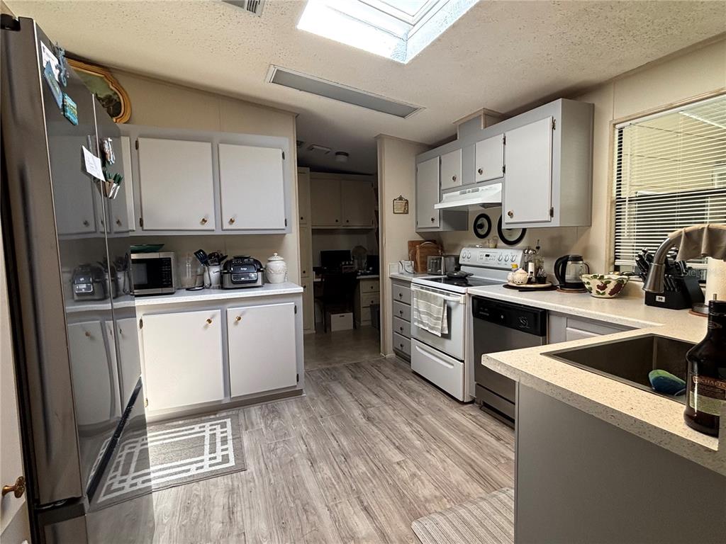 A kitchen features light gray cabinets, stainless steel appliances, a skylight, and wood-look flooring — 3725 COHEN DRIVE UNIT 717, ZELLWOOD, FL