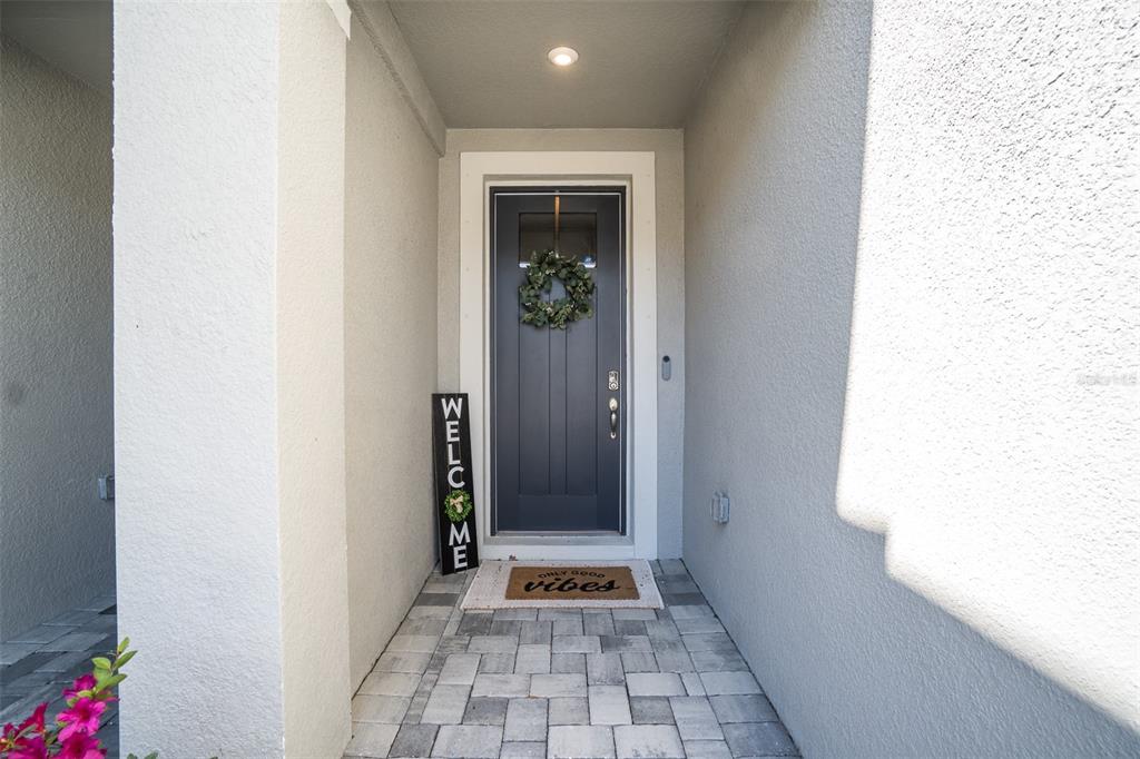 A gray front door with a wreath, welcome sign, and doormat on a paved porch — 8518 PRIMROSE WILLOW PLACE, ODESSA, FL