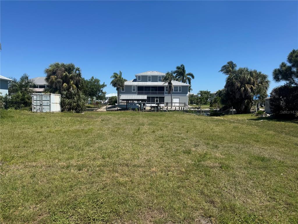A grassy lot faces a multi-story house with a dock on a canal — 24360 BLACKBEARD BLVD, PUNTA GORDA, FL
