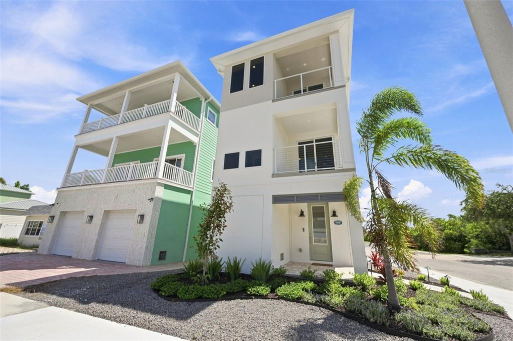 A modern three-story white house with balconies stands next to a green house with garages — 19101 GULF BOULEVARD, INDIAN SHORES, FL