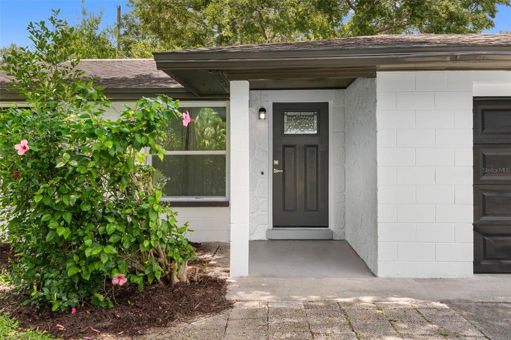 A white concrete block house exterior features a dark front door and a flowering bush — 11478 92ND STREET, LARGO, FL
