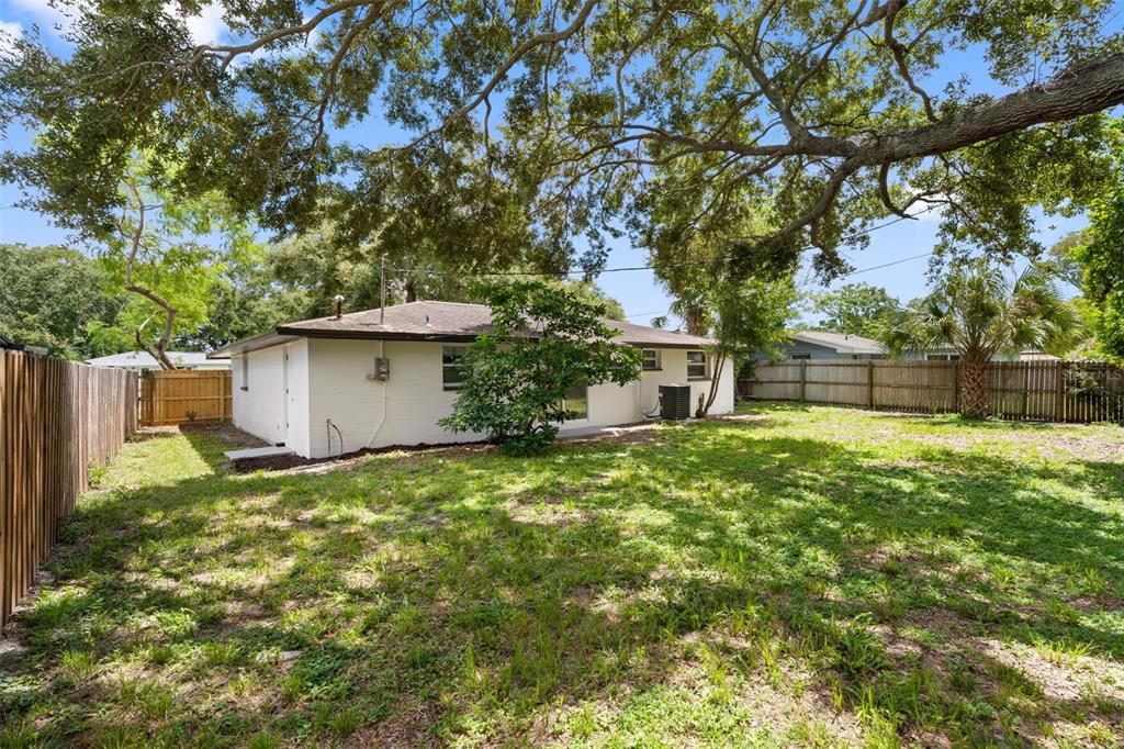 The backyard of a white house features a large tree, lawn, and wooden privacy fence — 11478 92ND STREET, LARGO, FL