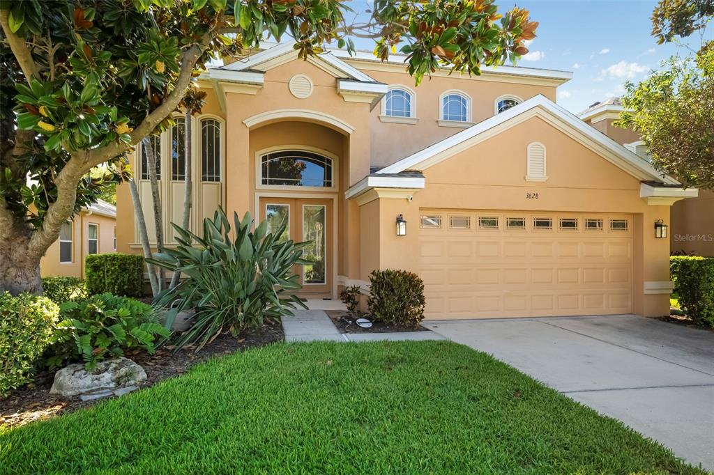 A two-story tan stucco house with a front-facing garage and a landscaped front yard — 3628 SUMMERWIND CIRCLE, BRADENTON, FL
