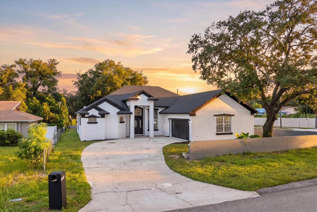 A white single-story house with a dark roof, a concrete driveway, and a large tree — 1222 N HART BOULEVARD, ORLANDO, FL