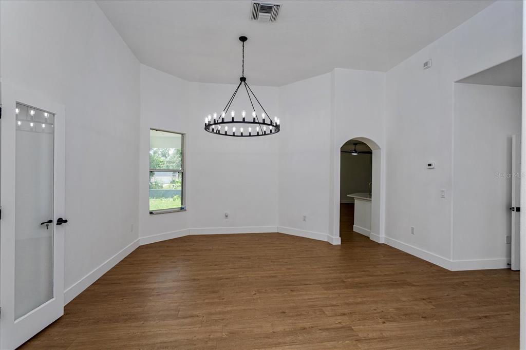 A bright dining room features wood-look flooring, white walls, and a large black chandelier — 1222 N HART BOULEVARD, ORLANDO, FL