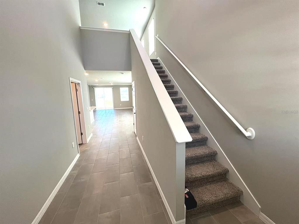 An entryway features a tiled floor, a carpeted staircase with a white railing, and high ceilings — 820 RIVERS CROSSING STREET, CLERMONT, FL