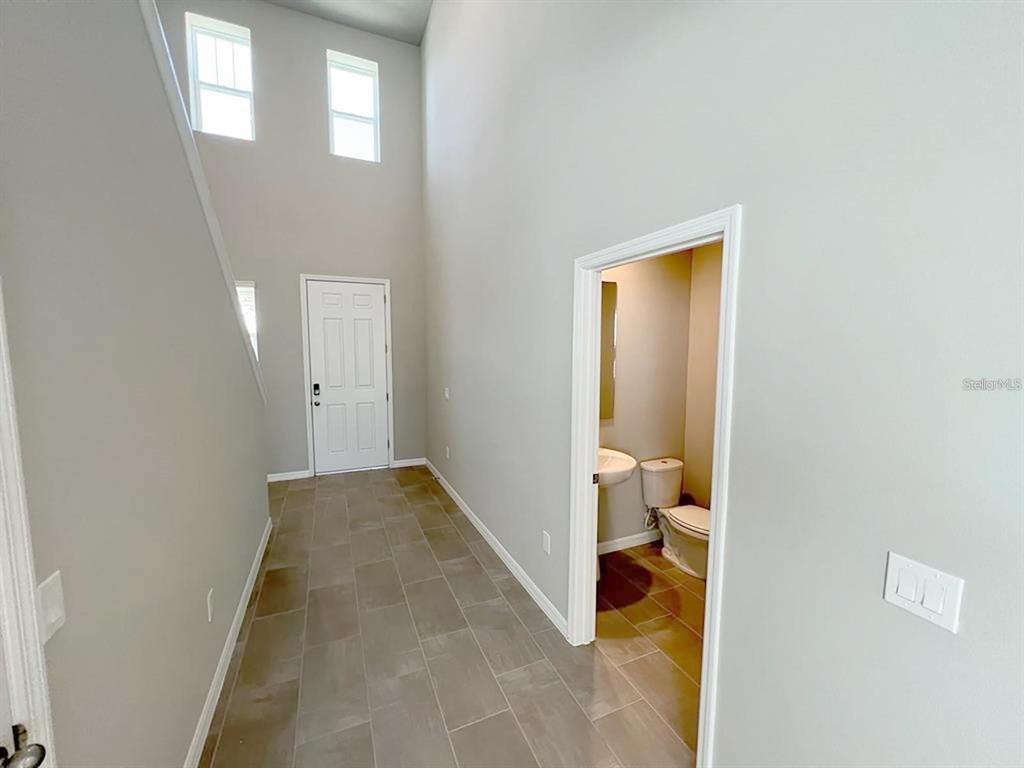 A tiled entryway features a high ceiling, a front door, and a small half bathroom — 820 RIVERS CROSSING STREET, CLERMONT, FL