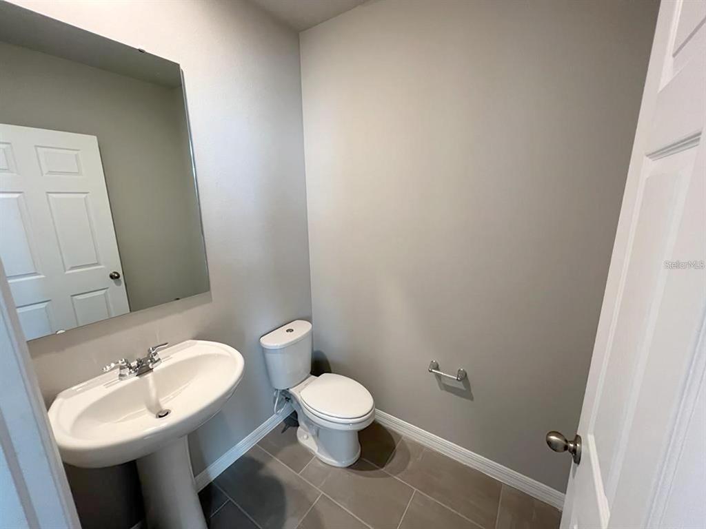 A small bathroom features a pedestal sink, a toilet, and a wall-mounted mirror — 820 RIVERS CROSSING STREET, CLERMONT, FL