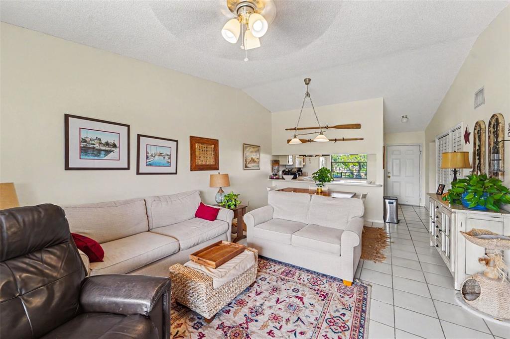 A living room features a television, a leather recliner, a sofa, and a balcony view — 1702 SEASCAPE CIRCLE UNIT 203, TARPON SPRINGS, FL