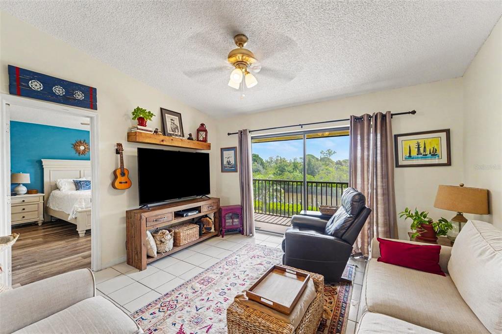 A living and dining area features a wood table, beige sofa, and a sliding glass door — 1702 SEASCAPE CIRCLE UNIT 203, TARPON SPRINGS, FL