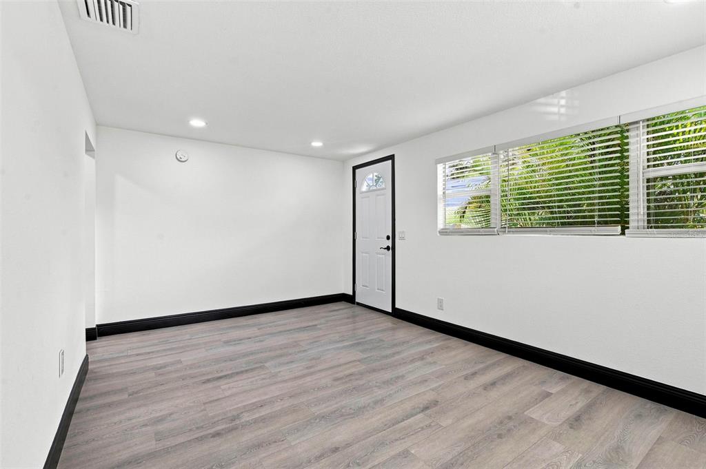 An empty room with white walls, black baseboards, light wood-look flooring, and a white door — 3611 3RD AVENUE S, ST PETERSBURG, FL