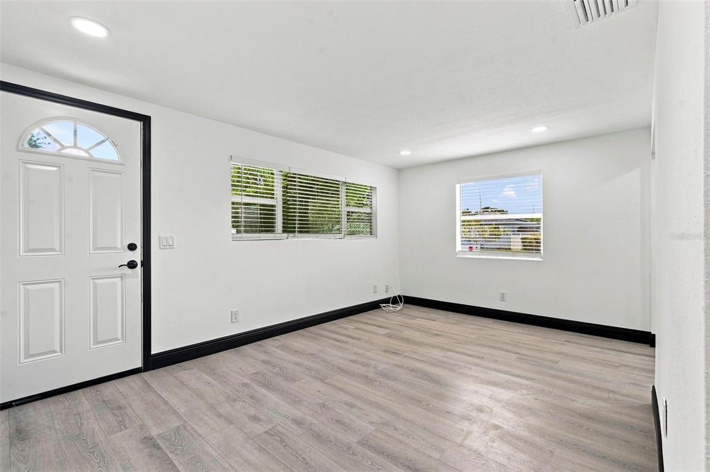 A bright, empty room features white walls, black trim, and light wood-look flooring — 3611 3RD AVENUE S, ST PETERSBURG, FL
