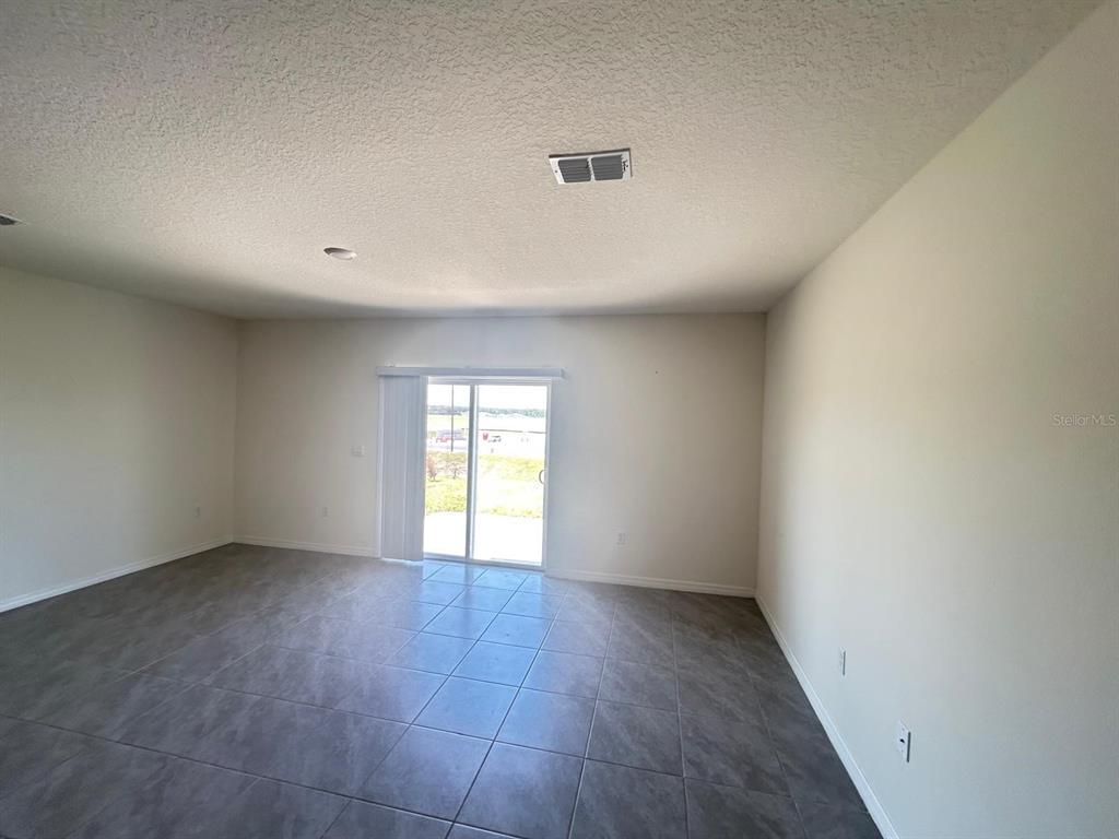 An empty room features gray tile flooring, light-colored walls, and a sliding glass door — 1471 PLANK PLACE, DAVENPORT, FL