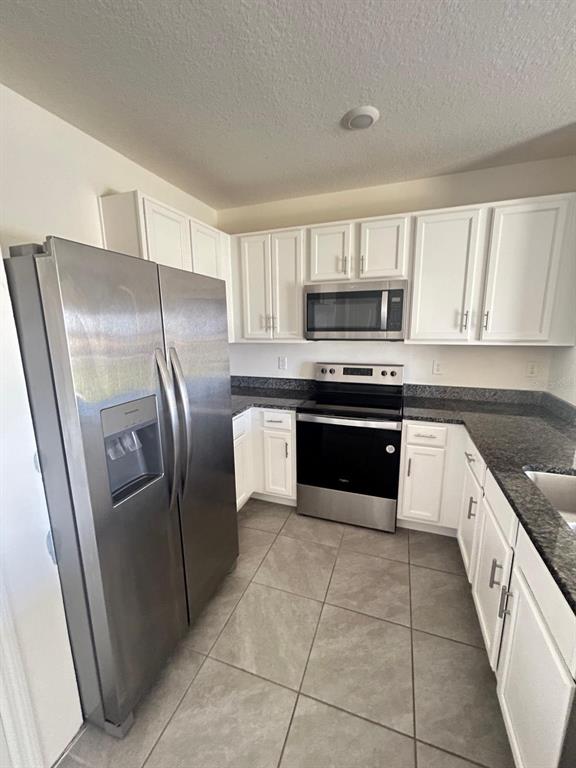 A kitchen features white cabinets, stainless steel appliances, and dark granite countertops — 1471 PLANK PLACE, DAVENPORT, FL