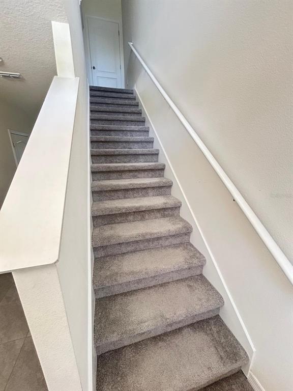 A carpeted staircase with a white handrail leads to a landing with a closed door — 1471 PLANK PLACE, DAVENPORT, FL
