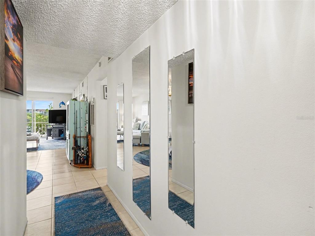 A hallway with tiled floors, two wall-mounted mirrors, and a view into a living area — 3915 LAKE BAYSHORE DRIVE UNIT 306, BRADENTON, FL