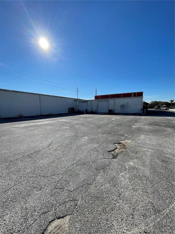 A large, paved parking lot sits in front of a white metal industrial warehouse building — 349 PLAZA DRIVE, EUSTIS, FL