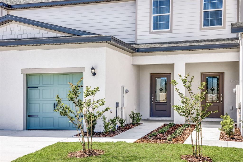 A two-story townhouse exterior with a light blue garage door and two front entry doors — 715 POPPY LANE, DUNDEE, FL