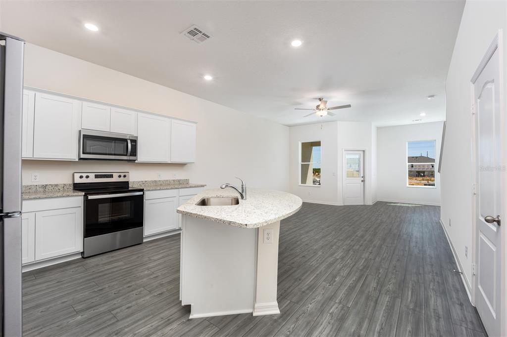 A kitchen with white cabinets, granite countertops, a center island, and gray wood-look flooring — 715 POPPY LANE, DUNDEE, FL