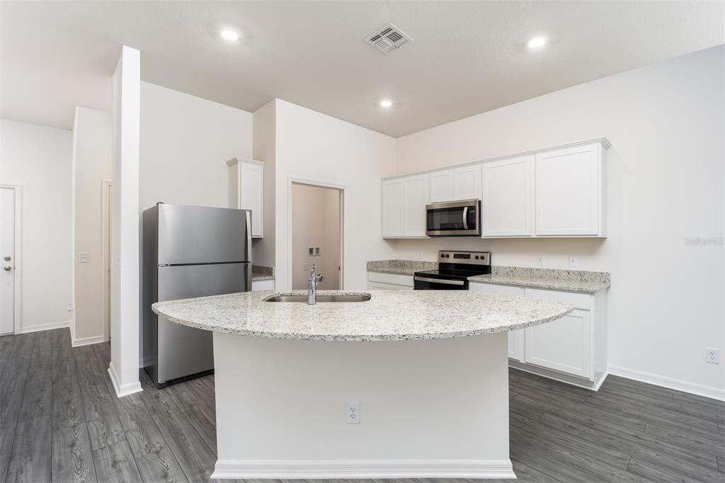 A kitchen features white cabinets, granite countertops, a central island with a sink, and appliances — 715 POPPY LANE, DUNDEE, FL