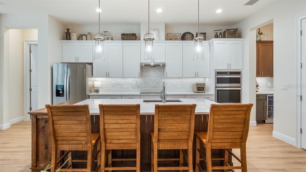 A kitchen features white cabinetry, a large island with four wooden stools, and stainless appliances — 4008 PINNACLE PLACE COURT, LADY LAKE, FL