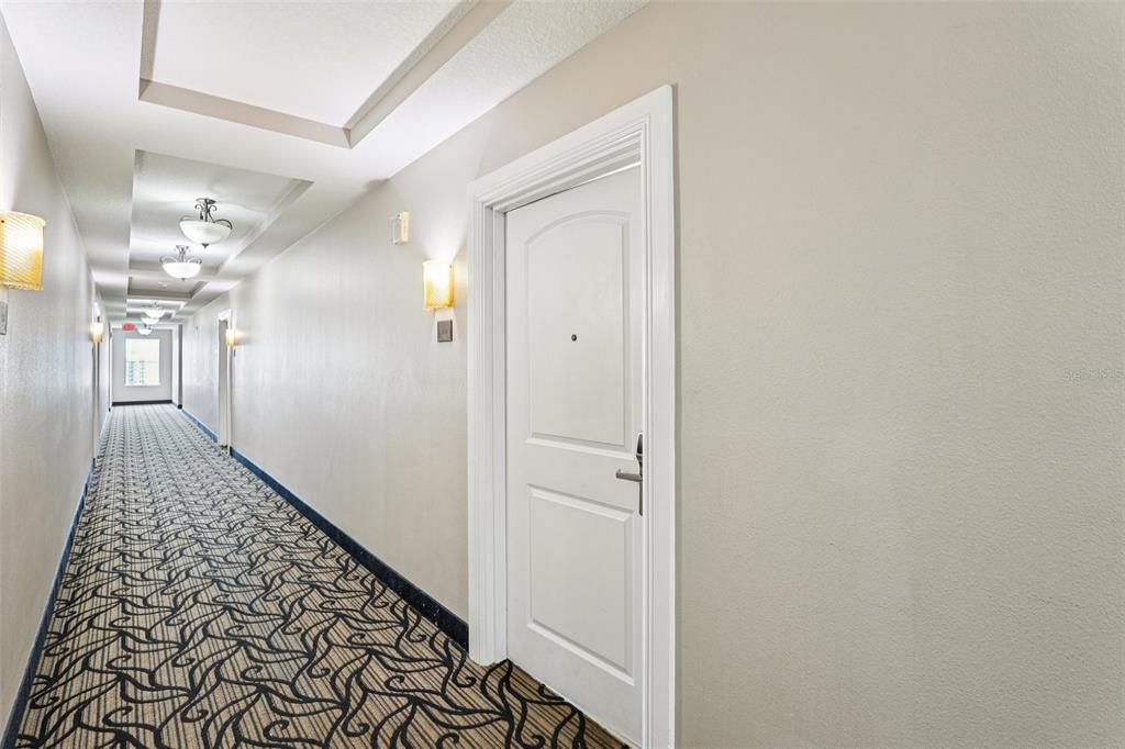 A long hotel-style hallway features patterned carpet, recessed lighting, and a white door — 7383 UNIVERSAL BOULEVARD UNIT 910, ORLANDO, FL