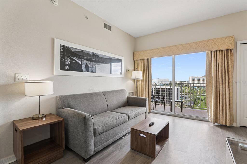 A living room features a gray sofa, a wood side table, and a balcony view — 7383 UNIVERSAL BOULEVARD UNIT 910, ORLANDO, FL