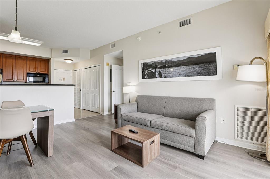 A living room features a grey sofa, a wooden coffee table, and an adjacent kitchen — 7383 UNIVERSAL BOULEVARD UNIT 910, ORLANDO, FL