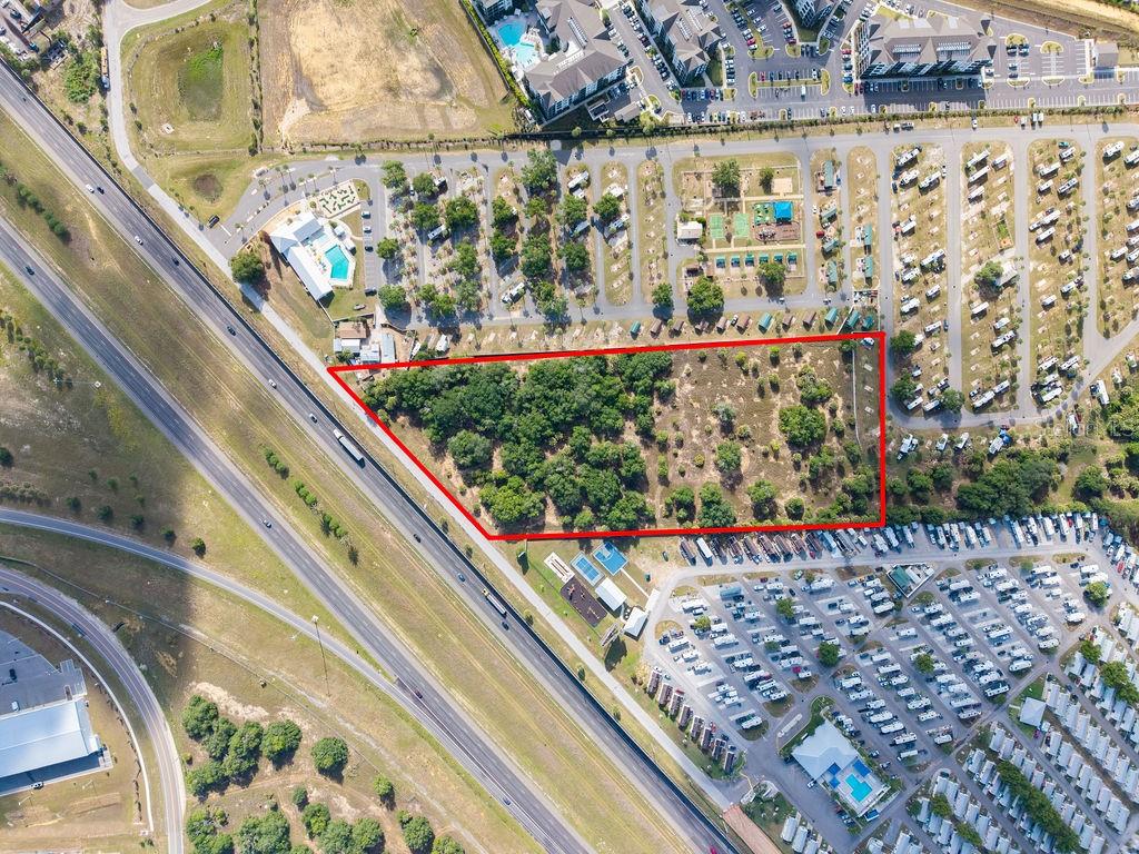 An aerial view shows a vacant, tree-covered lot outlined in red next to a highway — PRIME FRONTAGE, DAVENPORT, FL