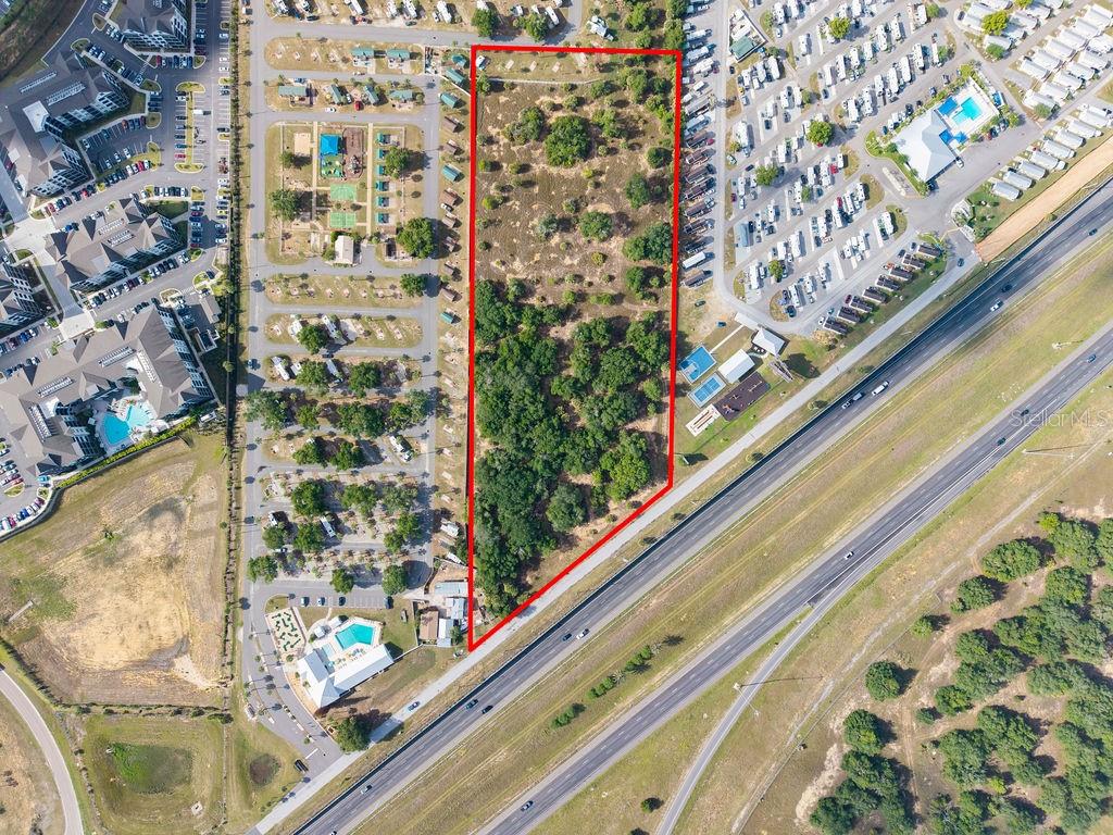 An aerial view shows a rectangular, tree-covered vacant lot outlined in red next to a highway — PRIME FRONTAGE, DAVENPORT, FL