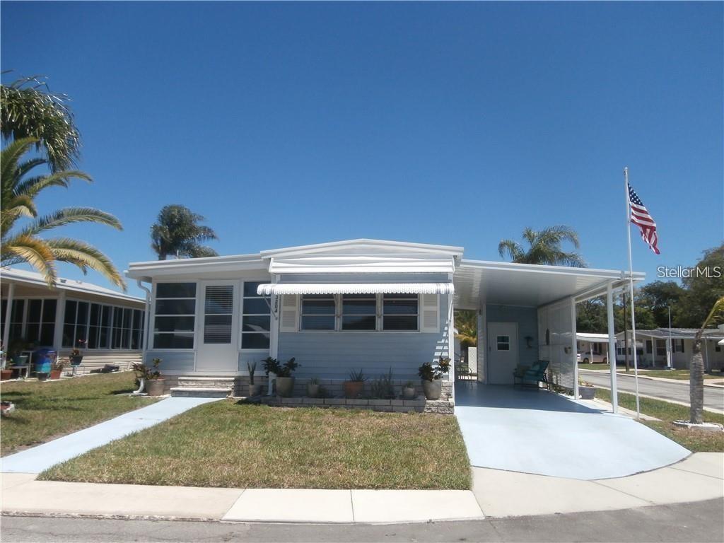 A light blue mobile home features a front porch, a carport, and a flag pole — 3204 CHANNING DRIVE, HOLIDAY, FL