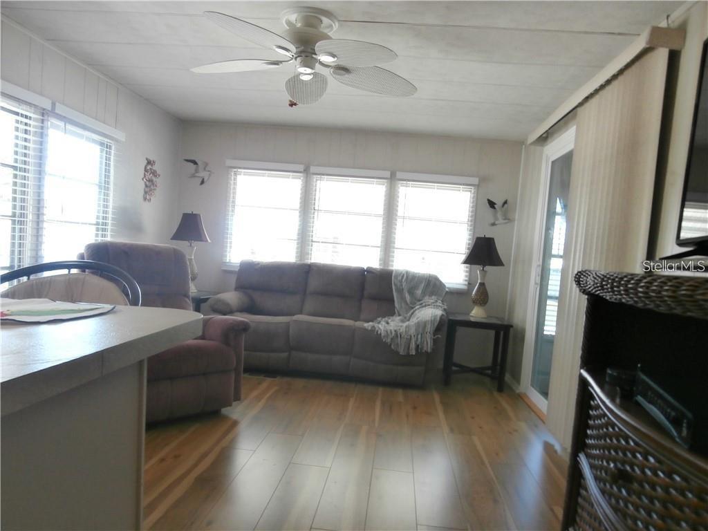 A living room features wood-look flooring, a ceiling fan, a sofa, and a recliner — 3204 CHANNING DRIVE, HOLIDAY, FL
