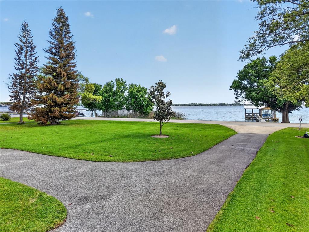 A paved driveway leads toward a lawn with trees overlooking a lake and boat dock — 1735 LAKESHORE DRIVE, MOUNT DORA, FL