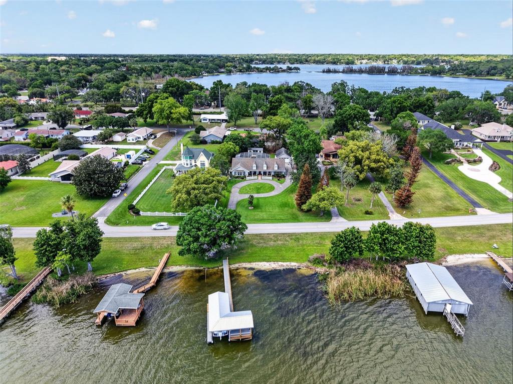 An aerial view shows a waterfront property with a house, lawn, and three boat docks — 1735 LAKESHORE DRIVE, MOUNT DORA, FL