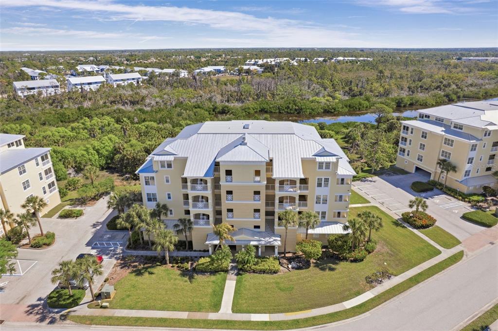 An aerial view shows a multi-story yellow apartment building surrounded by palm trees and landscaping — 8561 AMBERJACK CIRCLE UNIT 302, ENGLEWOOD, FL