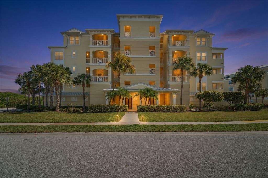 An aerial view shows multi-story apartment buildings surrounded by ponds, green space, and coastal water — 8561 AMBERJACK CIRCLE UNIT 302, ENGLEWOOD, FL