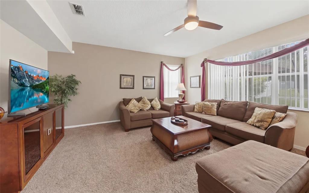 A living and dining area with beige walls, brown carpet, and a wooden dining set — 111 ALDRIDGE LANE, DAVENPORT, FL