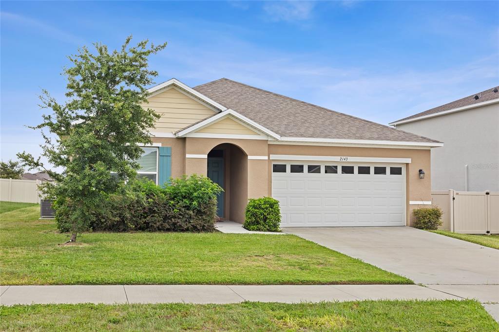 A single-story suburban house features a tan stucco exterior, a two-car garage, and landscaping — 2143 KALIN WAY, TAVARES, FL