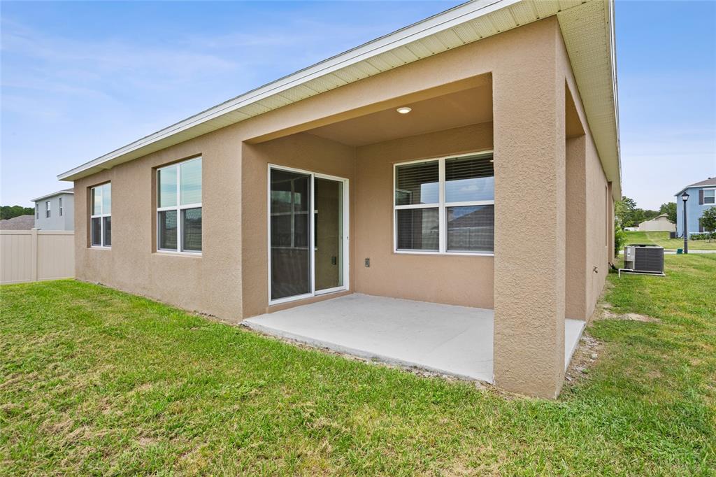 A tan stucco house features a covered concrete patio and a sliding glass door — 2143 KALIN WAY, TAVARES, FL