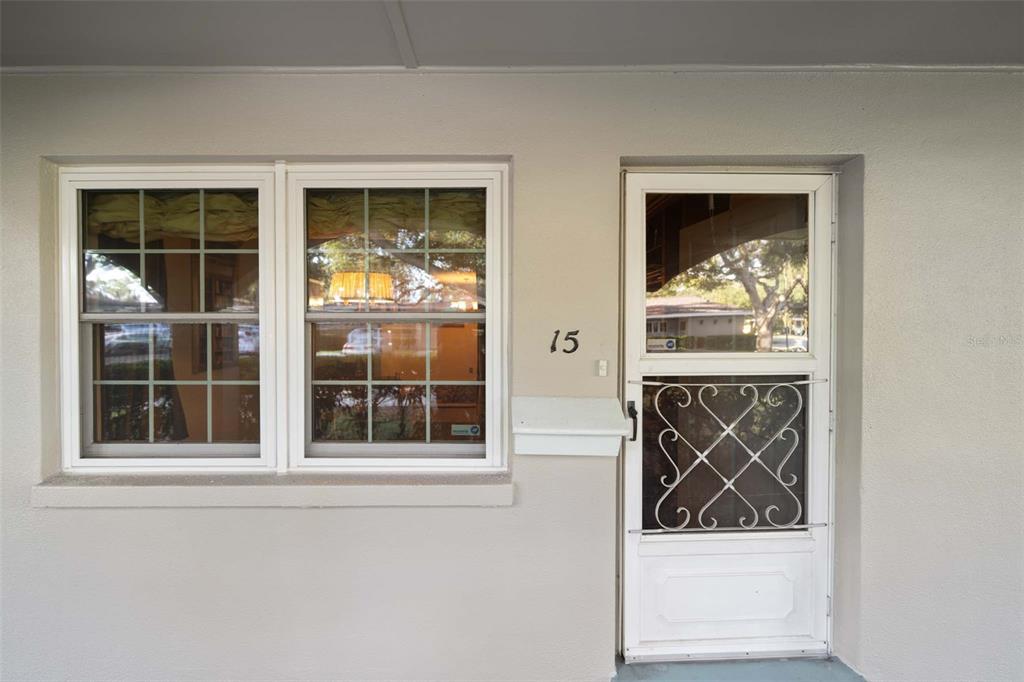 The exterior of a residential unit features a white front door with a screen and windows — 11200 102ND AVENUE UNIT 15, SEMINOLE, FL