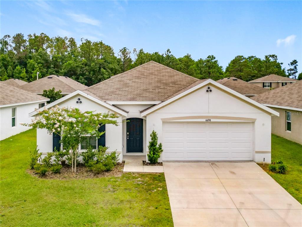 A single-story house with a white stucco exterior, a two-car garage, and a brown shingled roof — 6698 SE 3RD LOOP, OCALA, FL