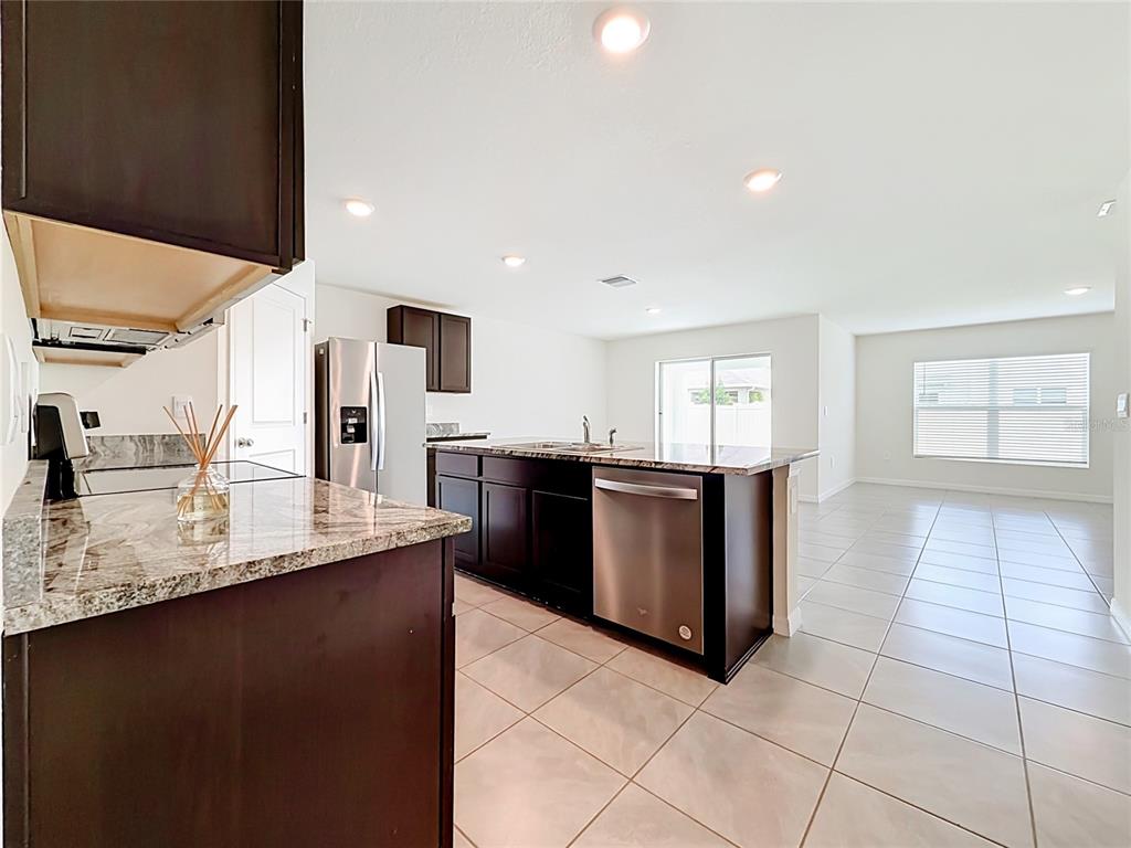 A kitchen with dark cabinets, granite countertops, and stainless steel appliances opens to a living area — 6698 SE 3RD LOOP, OCALA, FL